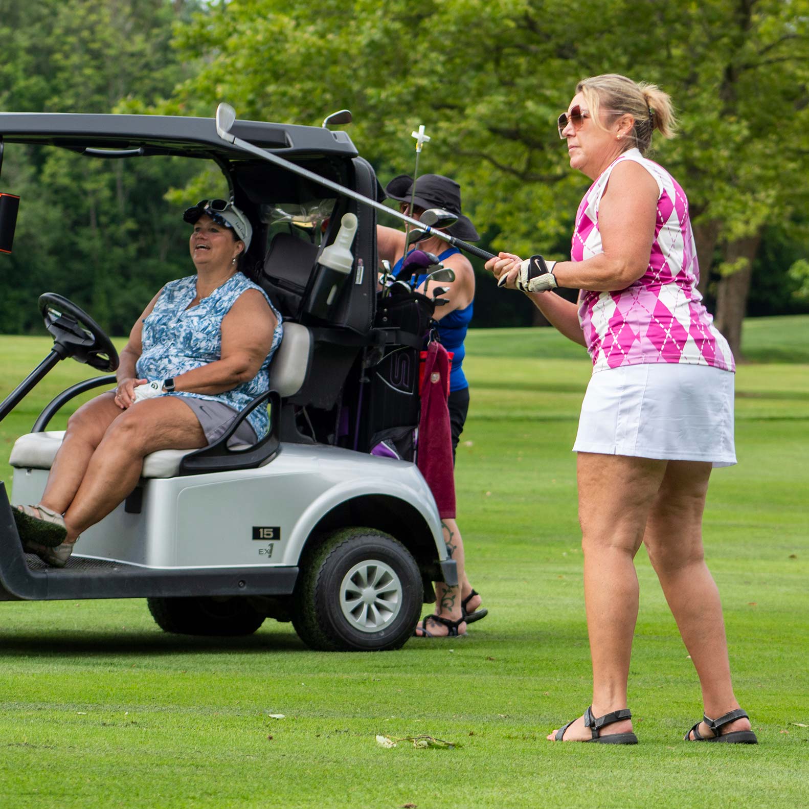A golfer watches their ball fly as their teammate looks on